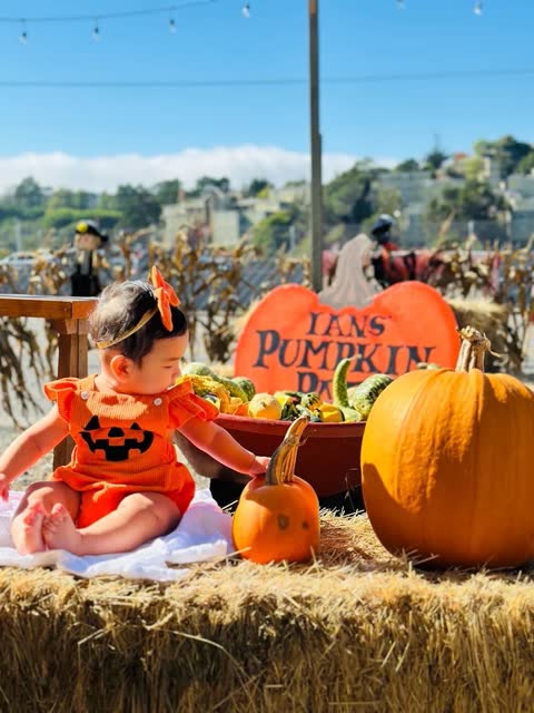 A baby in a pumpkin costume poses beside the Ian's Pumpkin Patch sign